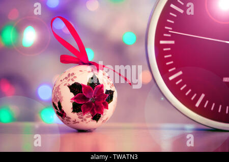 Red clock with speedy blurred effect. Concept of fast time passing. Christmas tree toy lies on the table next to the red clock on the background of th Stock Photo