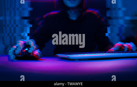 Hacker in the hood working with computer typing text in dark room. Image with glitch effect Stock Photo