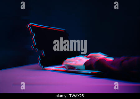 Hacker in the hood working with laptop typing text in dark room. Image with glitch effect Stock Photo