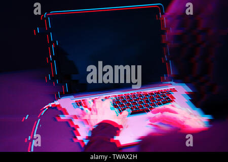 Hacker in the hood working with laptop typing text in dark room. Image with glitch effect Stock Photo