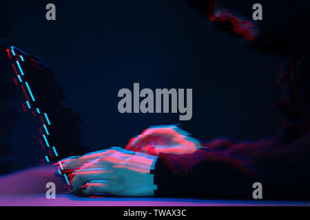 Hacker in the hood working with laptop typing text in dark room. Image with glitch effect Stock Photo