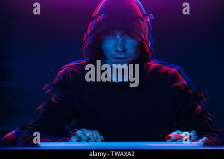 Hacker in the hood working with computer typing text in dark room. Image with glitch effect Stock Photo
