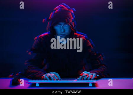 Hacker in the hood working with computer typing text in dark room. Image with glitch effect Stock Photo