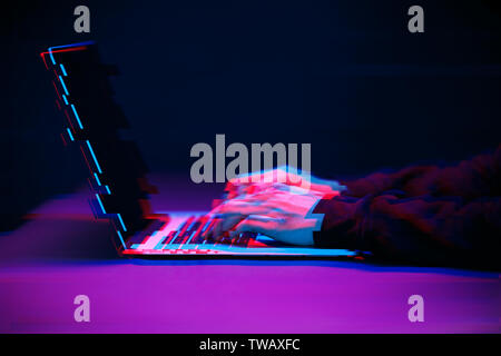 Hacker in the hood working with laptop typing text in dark room. Image with glitch effect Stock Photo