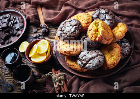 Crinkle cookies. Cracked lemon and chocolate biscuits on an earthenware plate on a rustic wooden table with ingredients, close-up Stock Photo