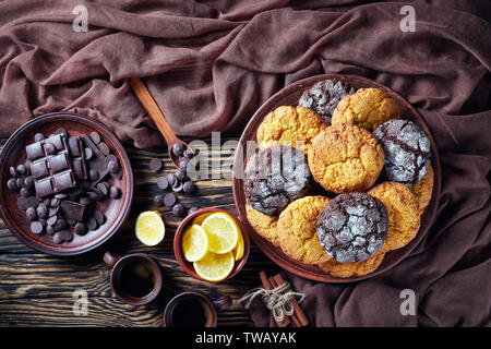 overhead view of Crinkle cookies. Cracked lemon and chocolate biscuits on an earthenware plate on a rustic wooden table with ingredients, flat lay Stock Photo