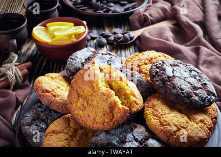 Crinkle cookies. Cracked lemon and chocolate biscuits on an earthenware plate on a rustic wooden table with ingredients, view from above, close-up Stock Photo