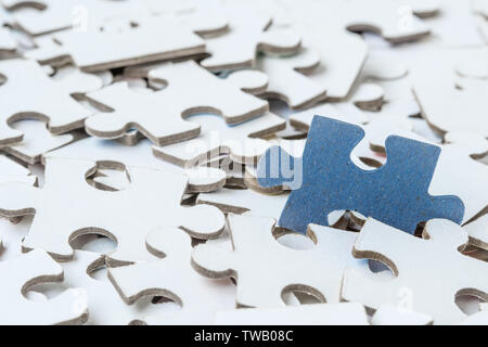 Oneblue piece of puzzle on pile of white jigsaw puzzles Stock Photo