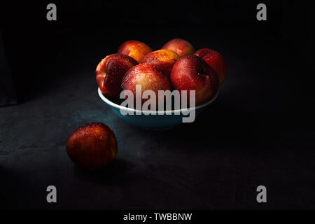 Still life of fresh delicious sweet nectarines with droplets of water in a bowl on dark background. Low key. Stock Photo