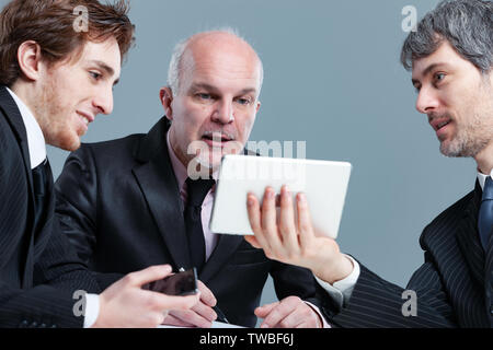 Three businessman having an animated discussion over information on a small tablet as they sit around a table in a meeting Stock Photo