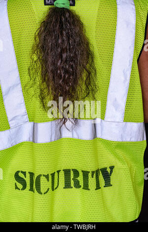 A female security guard with a ponytail,  wearing a high visibility fluorescent yellow-green safety vest Stock Photo