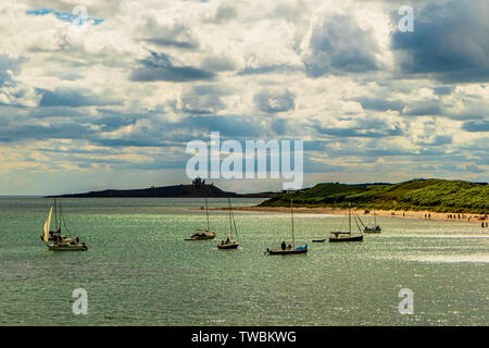 Leisure boats moored in the bay at Low Newton-by-the-Sea, with the ruins of Dunstanburgh Castle behind. Northumberland, UK. August 2018. Stock Photo