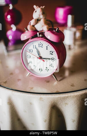 Vertical photo of a children's pink alarm clock on a bedside table. Stock Photo