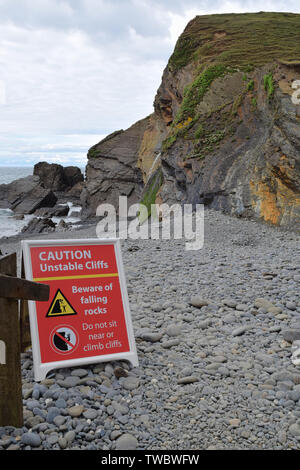 Warning sign under cliff base on beach regarding the danger of unstable cliff and falling rocks Stock Photo