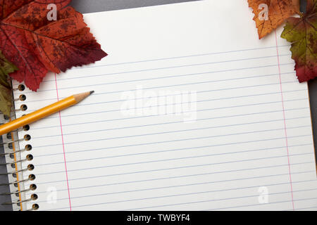 close up view of a empty page in a lined spiral bound notebook with yellow pencil and autumn leaves Stock Photo