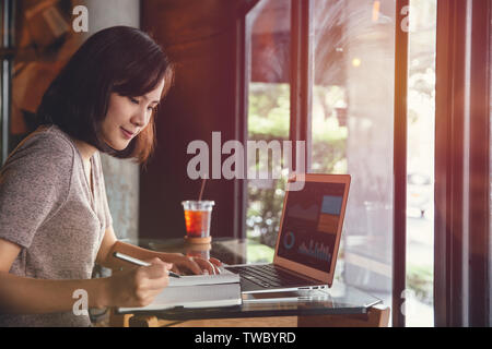Isolated mockup image of laptop and Young business woman in casual dress sitting at table in cafe and writing in notebook. Freelancer working in coffe