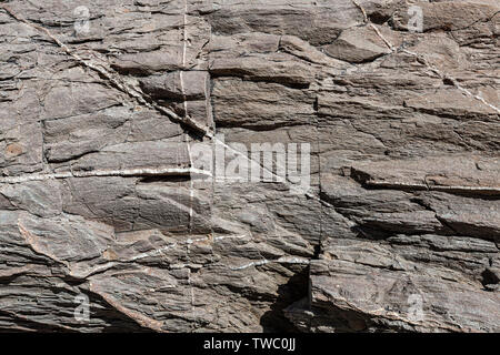 Texture of the surface of the natural rock, where you can see the layers of rock and lines of white crystals formed over time. Stock Photo