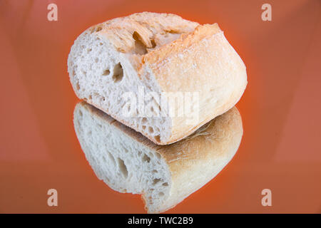 Close-up of a delicious and fresh slice of baguette, on a mirror, isolated in an orange background. Stock Photo