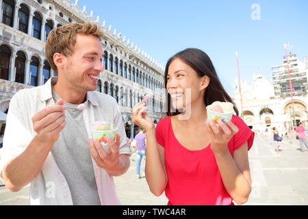 Couple eating ice cream on vacation travel in Venice, Italy. Smiling happy young couple in love having fun eating italian gelato food outdoors during holidays on San Marco Square, Venice, Italy Stock Photo