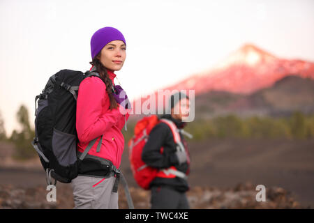 Hiking people on mountain. Hiker couple walking with backpack in high altitude mountains. Young woman hiker in focus trekking at sunset Tenerife, Canary Islands, Spain. Stock Photo
