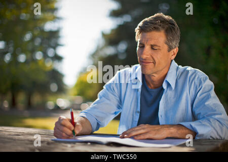 Middle aged man writing in a notebook at the park. Stock Photo