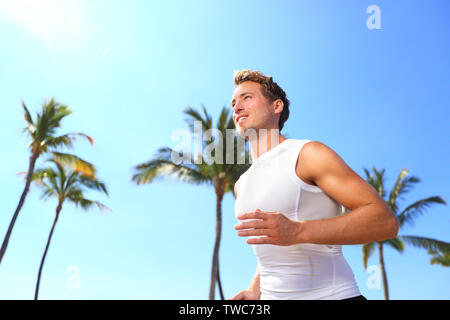 Sport man running. Male athlete runner jogging in compression t-shirt top training on palm trees beach. Fit handsome male fitness model jogging alone training for marathon run. Man in his twenties. Stock Photo