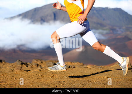 Trail running - male runner in cross country run. Closeup of strong legs and running shoes sprinting at speed. Male athlete fitness runner in compression sports clothing, socks and shorts. Stock Photo