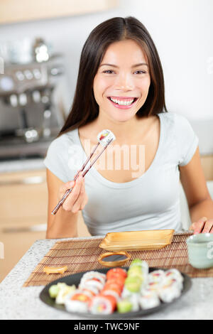 Sushi eating pretty mixed race young Asian and Caucasian woman - smiling happily holding chopsticks enjoying a maki sushi. Healthy lifestyle Stock Photo