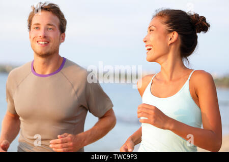 Jogging fitness young mixed race couple running happy smiling and laughing enjoying sports outdoors. Exercising multicultural people - young caucasian man and pretty asian model Stock Photo