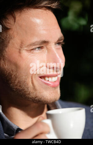 Man closeup portrait at cafe drinking coffee smiling happy. Handsome male model enjoying espresso at outdoor cafe in sun. Stock Photo
