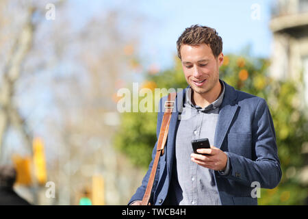 Young urban businessman professional on smartphone walking in street using app texting sms message on smartphone wearing jacket on Passeig de Gracia, Barcelona, Catalonia, Spain. Stock Photo