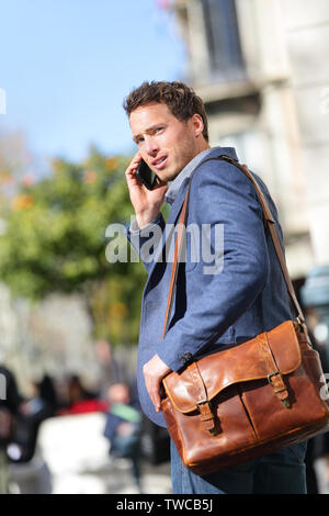 Business man on smartphone walking in street talking on mobile smart phone smiling wearing jacket and leather laptop bag on Passeig de Gracia, Barcelona, Catalonia, Spain. Stock Photo