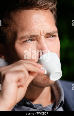 Espresso coffee - man drinking at cafe portrait. Handsome male drinking from espresso cup sitting outside at sidewalk cafe. Close up of male business man sitting outdoors in suit jacket. Stock Photo