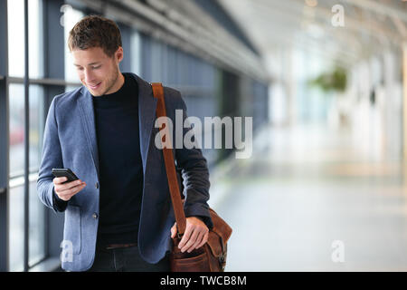 Man on smart phone - young business man in airport. Casual urban professional businessman using smartphone smiling happy inside office building or airport. Handsome man wearing suit jacket indoors. Stock Photo