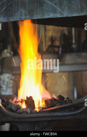 Close up of flames with male blacksmith forge at work making metal shapes in his blacksmith workshop, Hillsboro, Wisconsin, USA. Stock Photo