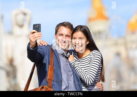 Lovers - young couple happy taking selfie photo with smart phone camera. Modern urban city man and woman having fun taking self portrait picture with smartphone, Catalonia Square, Barcelona, Spain Stock Photo