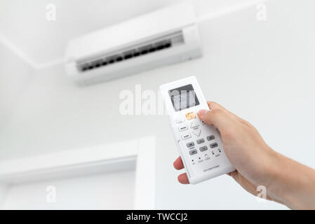 Air conditioner split on the wall inside the room. Man hand holding remote control Stock Photo