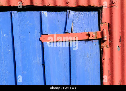 Section of shed door on croft with red corrugated wall and hinge, contrasting against bright blue door. Lochcarron, Highlands of  Scotland. Stock Photo