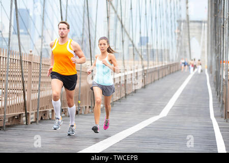 Running couple. Runners jogging outside on run. Asian woman and Caucasian man runner and fitness sport models training outdoors on Brooklyn Bridge, New York City, USA. Stock Photo