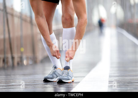 Running shoes - Runner man tying laces, New York City on Brooklyn Bridge. Male athlete runner and feet closeup. Fitness model wearing compression socks. Stock Photo