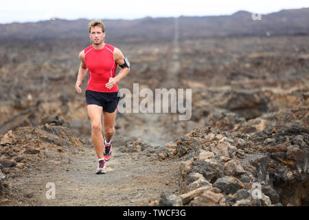Trail runner - running man trail runner cross country training outdoors for marathon or triathlon. Male athlete working out on Hawaii, Big Island, USA. Triathlete listening to music on smart phone Stock Photo