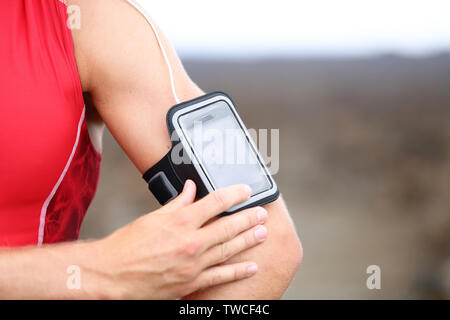Smart phone running music closeup - male runner listening to music adjusting settings on armband for smartphone. Fit man fitness model working out outside in red sporty outfit. Stock Photo
