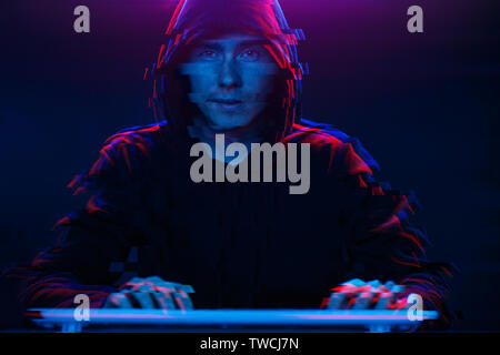 Hacker in the hood working with computer typing text in dark room. Image with glitch effect Stock Photo
