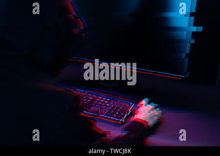 Hacker in the hood working with computer typing text in dark room. Image with glitch effect Stock Photo