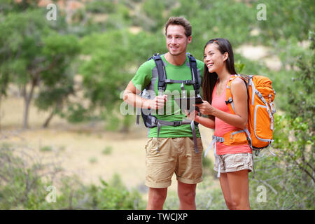Tablet computer - couple hiking using internet and tablet computer pc guide book app on hike in Zion National Park. Interracial active hiker couple, Asian woman, caucasian man trekking in Utah, USA.
