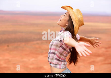 Cowgirl - woman happy and free on american prairie wearing cowboy hat with arms outstretched in freedom concept. Beautiful smiling multiracial Caucasian Asian young woman outdoors, Arizona Utah, USA. Stock Photo