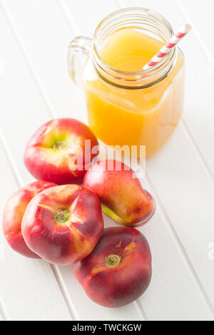 Ripe flat nectarines and juice glass on white table. Stock Photo