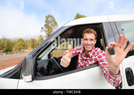 Car driver showing car keys and thumbs up happy. Young man holding car keys for new car. Rental cars or drivers licence concept with male driving in beautiful nature on road trip. Stock Photo