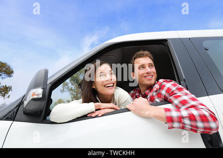 Couple lifestyle in new car looking out window. Driving young man and woman enjoying view on travel road trip in new car. Beautiful young multiracial young couple. Asian woman, Caucasian man. Stock Photo