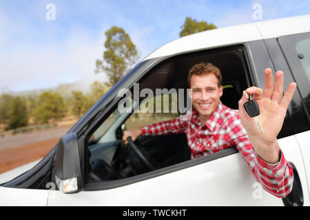 Car man driving rental car showing car keys happy looking at camera. Male driver on road trip in beautiful landscape nature. Focus on car key. Stock Photo